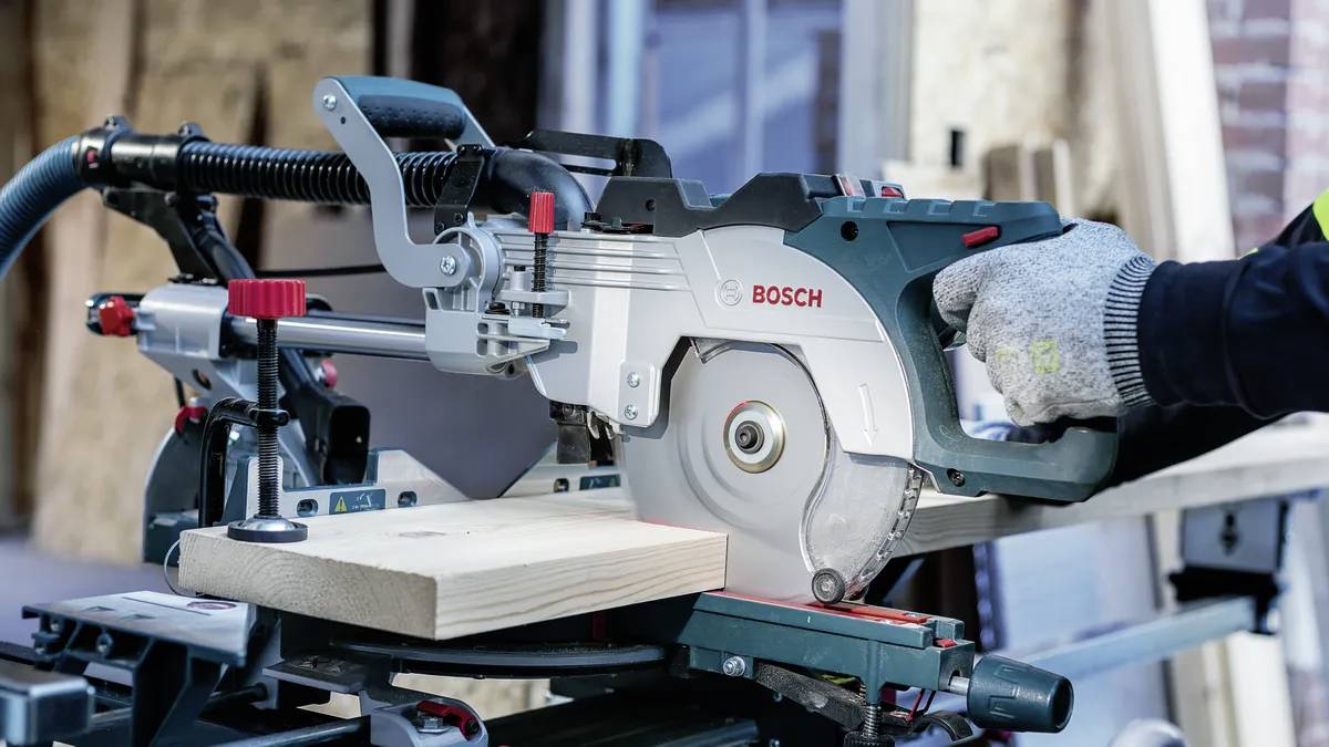 Eine Person mit Handschuhen bedient eine Bosch-Kreissäge, um eine Holzplanke zu schneiden, wobei Sicherheit und Präzision beim Holzarbeiten betont werden.