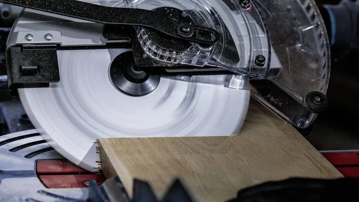 Eine Kreissäge, die durch eine Holzplanke schneidet, wobei Sägespäne sichtbar sind. Die Sägeblatt dreht sich schnell und verdeutlicht einen Holzbearbeitungsprozess.