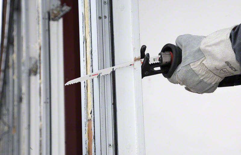 Eine Person sägt mit einer elektrischen Säbelsäge ein weißes Metallstück. Die Person trägt graue Arbeitshandschuhe.