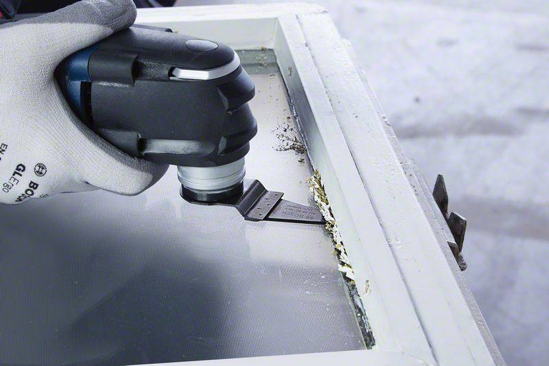 Eine Person entfernt mit einem Multitool-Powergerät alte Farbe von einer Fensterrahmenkante.