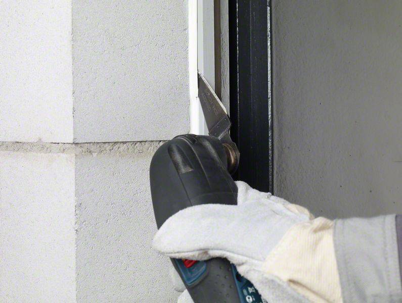 Eine Person trägt einen Handschuh und hält ein elektrisches Werkzeug, um einen weißen Abschnitt zwischen zwei Wandteilen zu bearbeiten.