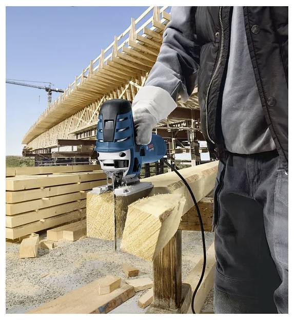 Ein Bauarbeiter, der eine blaue Kreissäge verwendet, um ein Stück Holz auf einer Baustelle mit Balken und Gerüsten im Hintergrund zu schneiden.