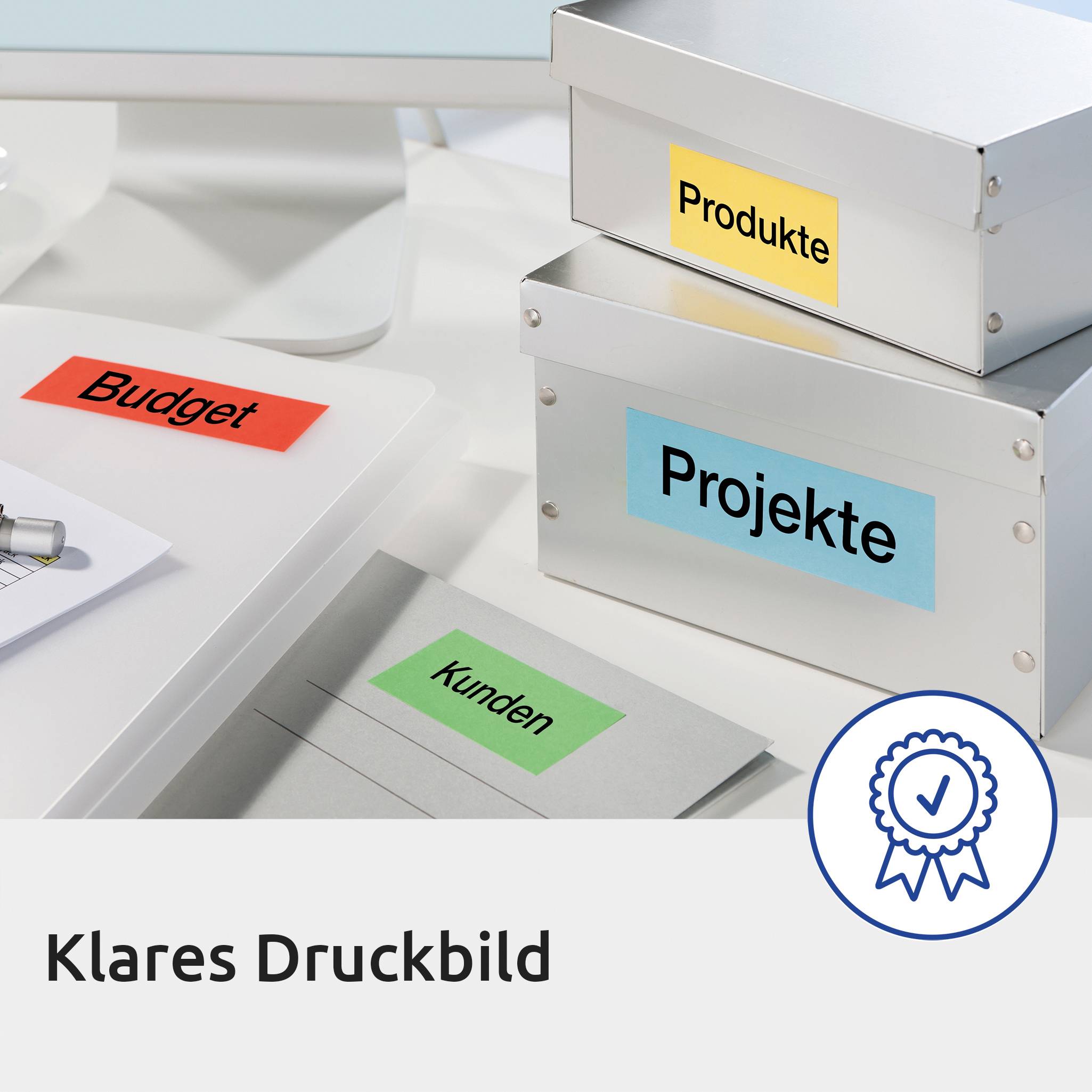 Drei beschriftete Boxen mit den Texten 'Produkte', 'Projekte' und 'Budget' auf einem Schreibtisch. Qualitätssiegel in der Ecke.