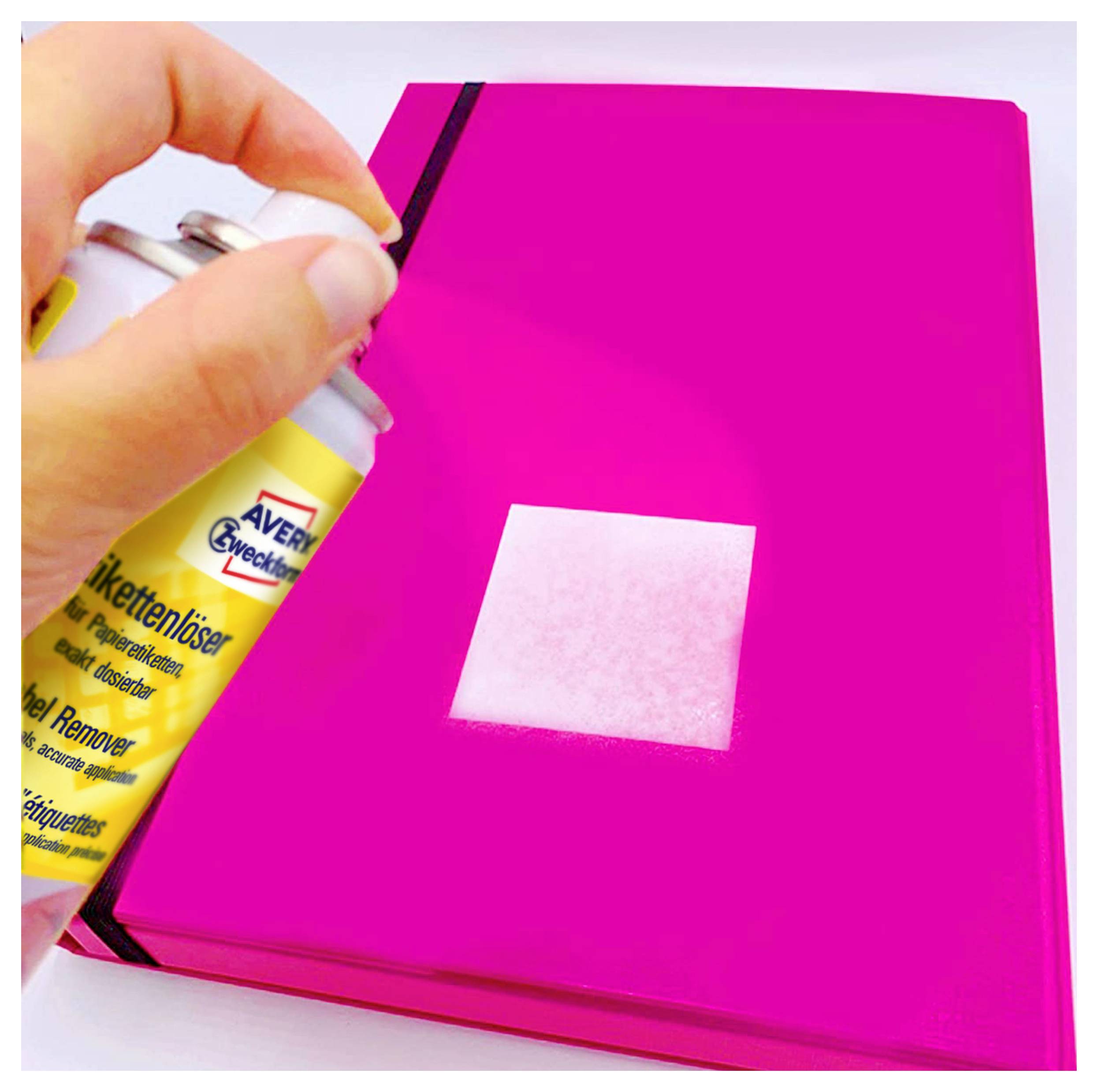 Hand sprüht Etikettenlöser auf ein helles Quadrat auf einem pinken Ordner oder Buch.