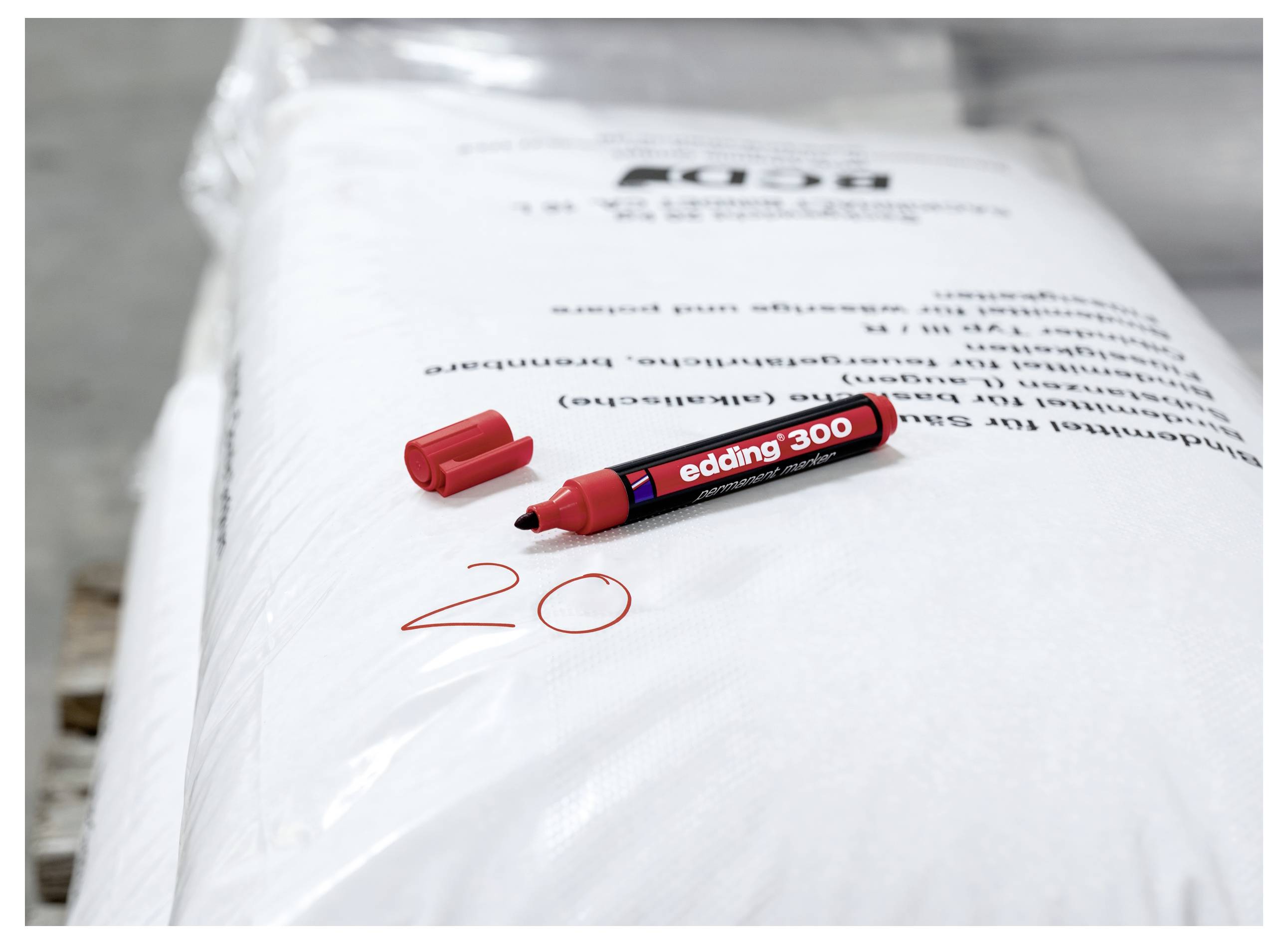 Roter Marker mit Kappe, der auf einer weißen Verpackung ruht, mit der handschriftlich in Rot geschriebenen Zahl „20" auf der Kunststofffolie.