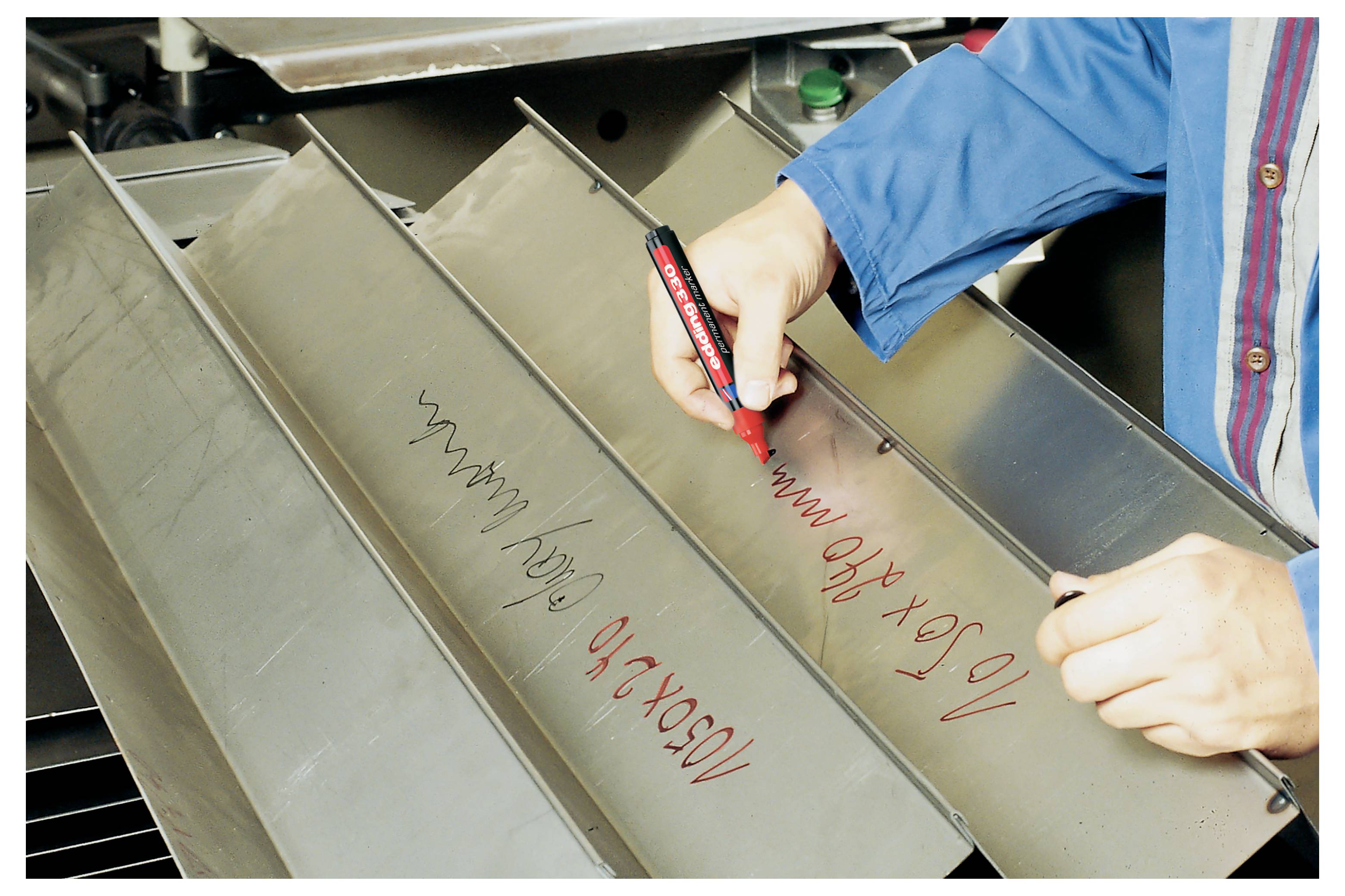 Ein Arbeiter in einer blauen Jacke markiert rote Inspektionsnotizen auf einem Metallmaschinenpanel mit einem schwarzen Marker.