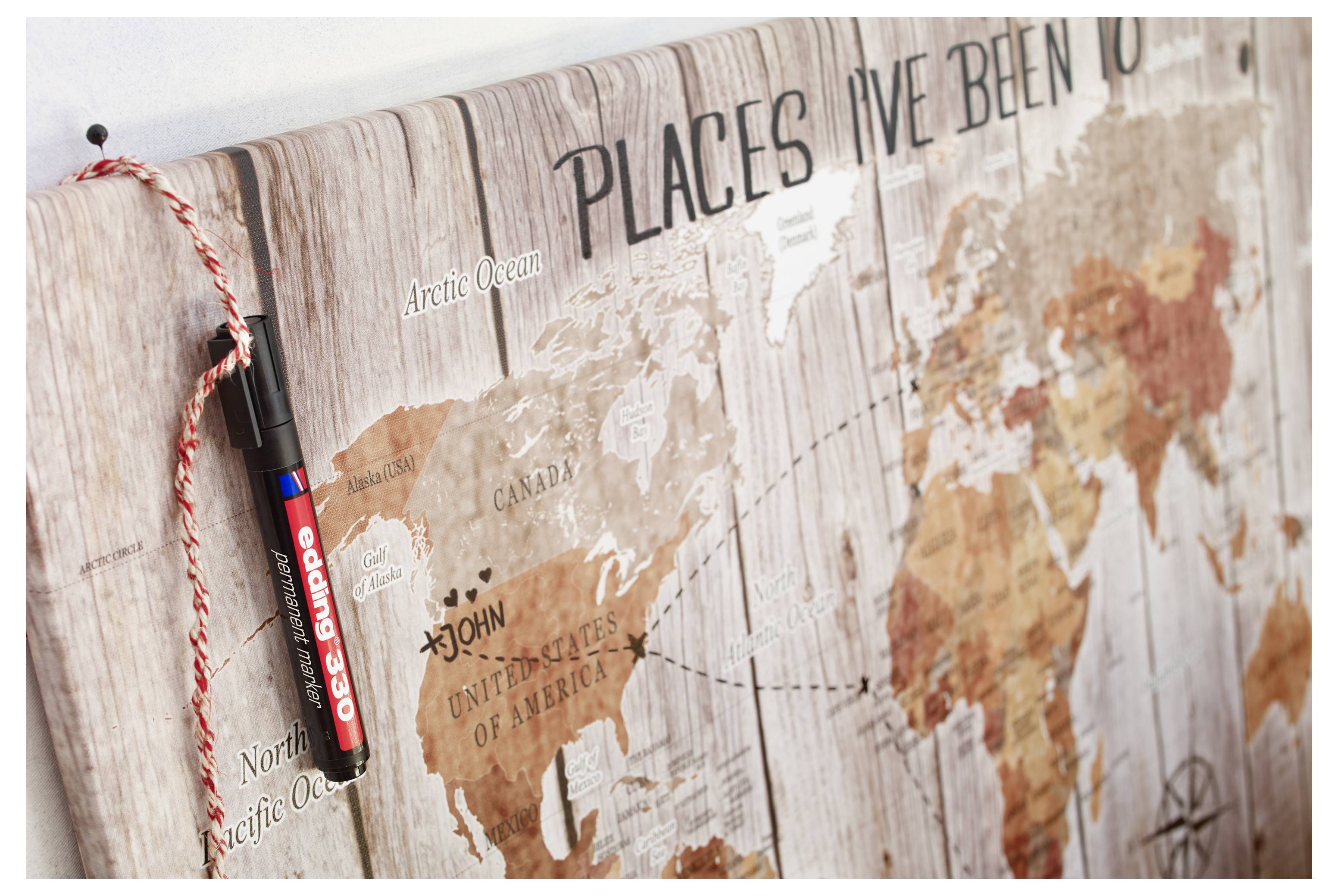 Nahaufnahme eines hölzernen Wanddrucks mit einer Weltkarte mit dem Titel „Places I've Been" (Orte, an denen ich gewesen bin) mit einem daneben hängenden rot-schwarzen Marker zum Markieren besuchter Orte.