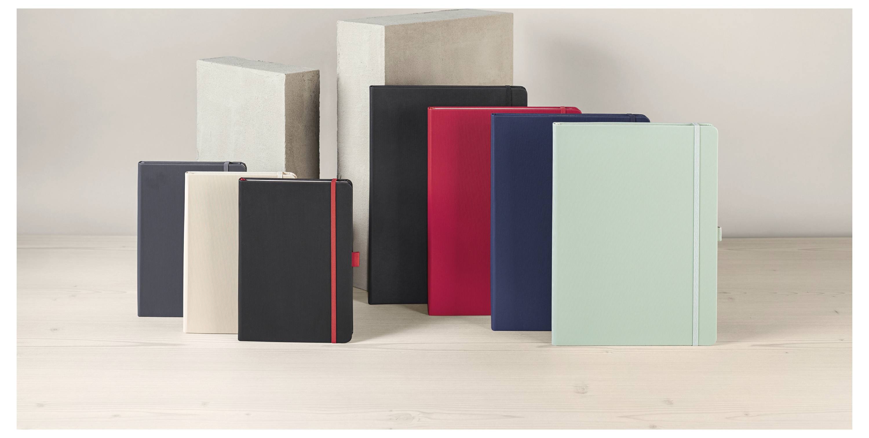 Assortierte Hardcover-Notizbücher in verschiedenen Größen und Farben auf einer hellen Holzoberfläche angeordnet