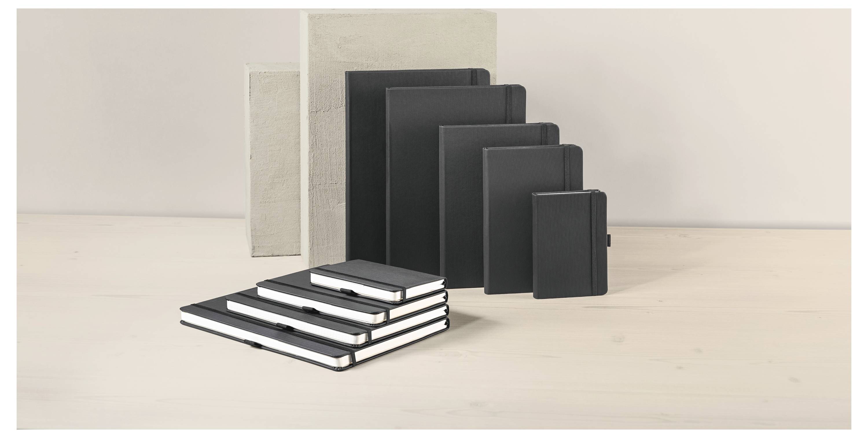 Sortierte leere Notizbücher und Journale in Schwarz, Creme und Grau auf einer hellen Holzoberfläche