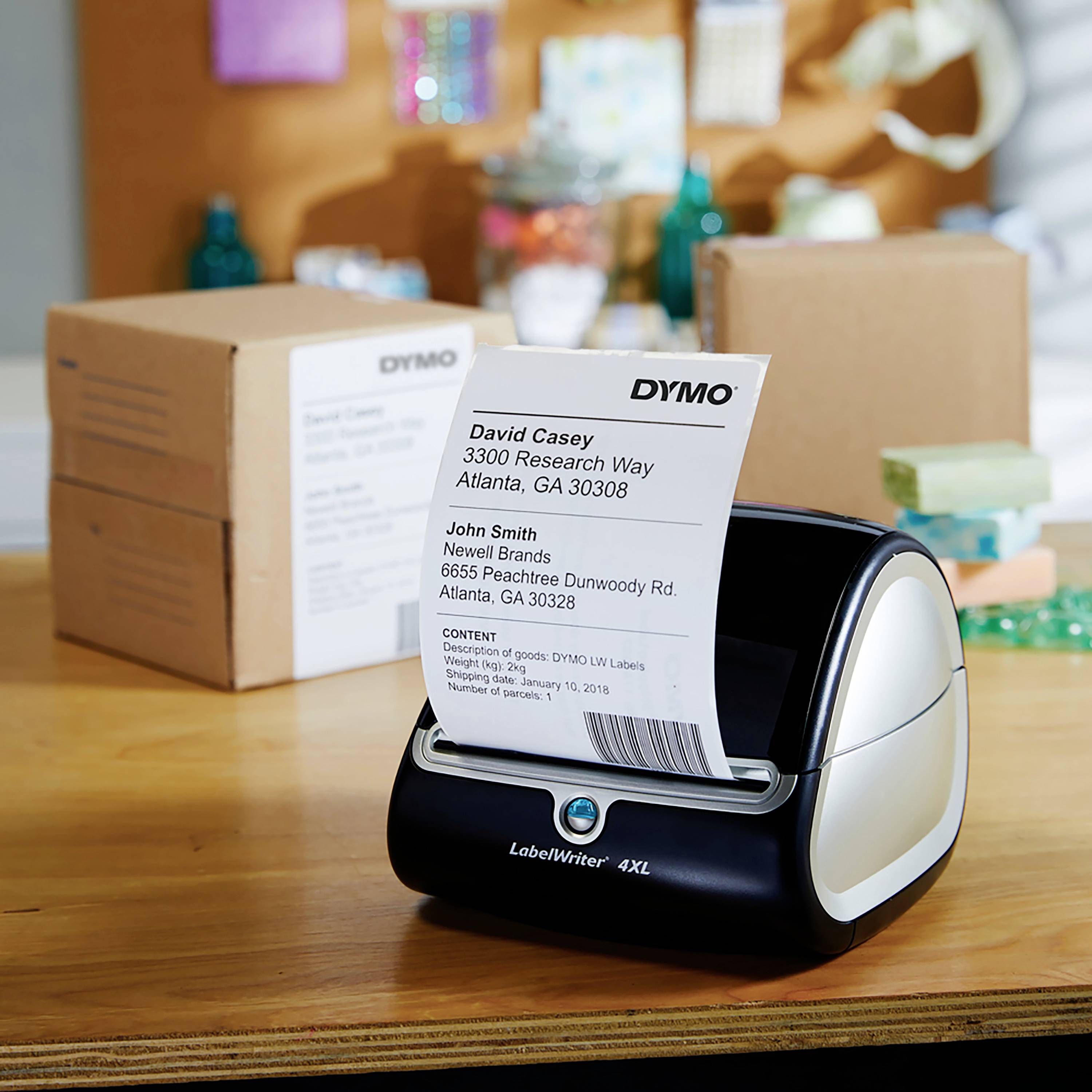 Ein Etikettendrucker druckt ein Adressetikett. Im Hintergrund sind Verpackungskartons zu sehen. Hauptfokus auf den Druckvorgang.