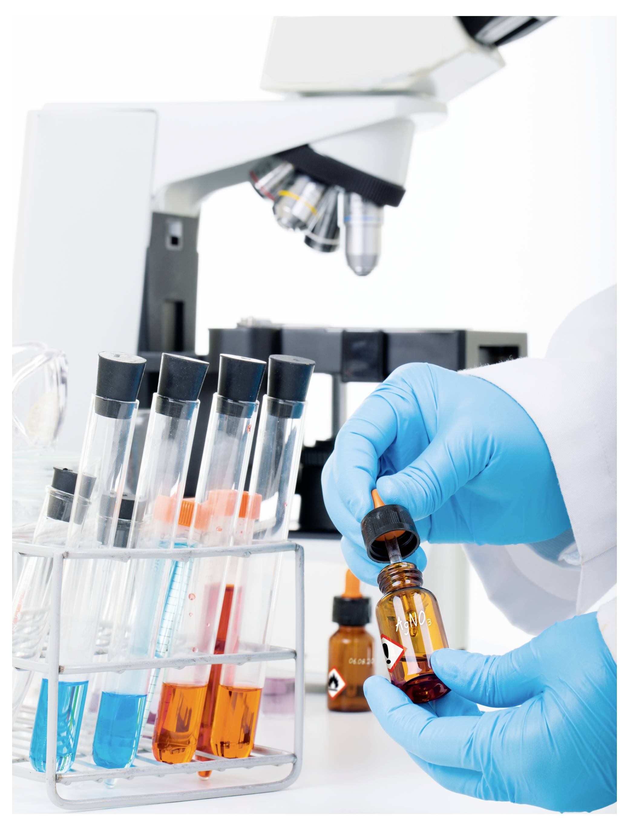 Handschuhtragende Labortechnikerin, die ein braunes Chemiefläschchen neben Reagenzgläsern unter einem Mikroskop in einem Labor behandelt.