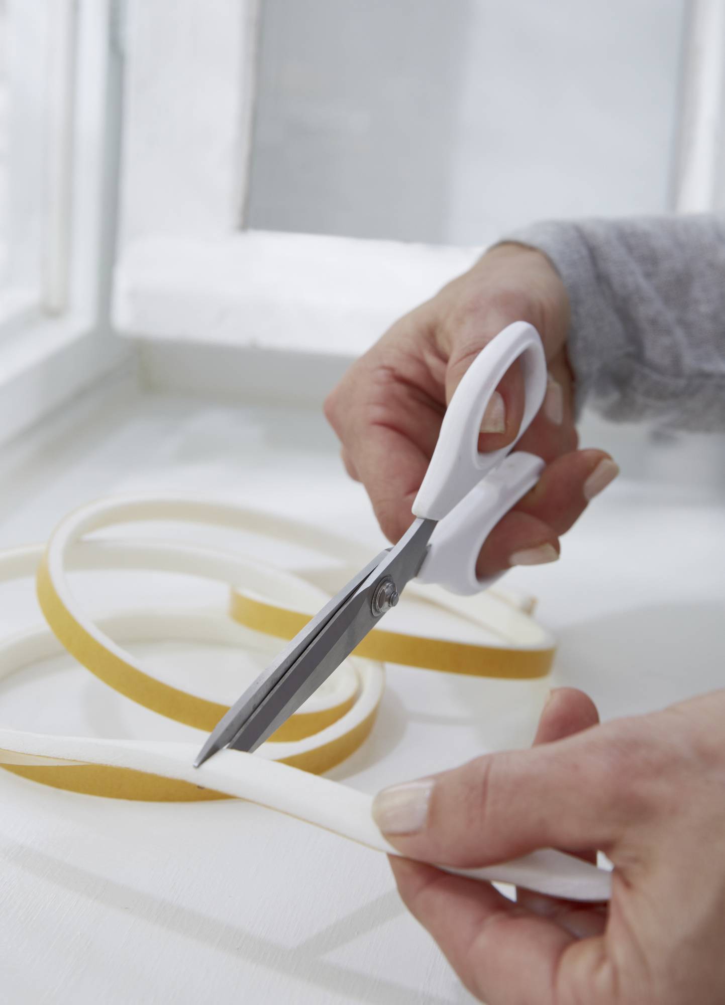 Person schneidet weißen Dichtungsschaum mit einer Schere; der Schaum liegt auf einer weißen Oberfläche.