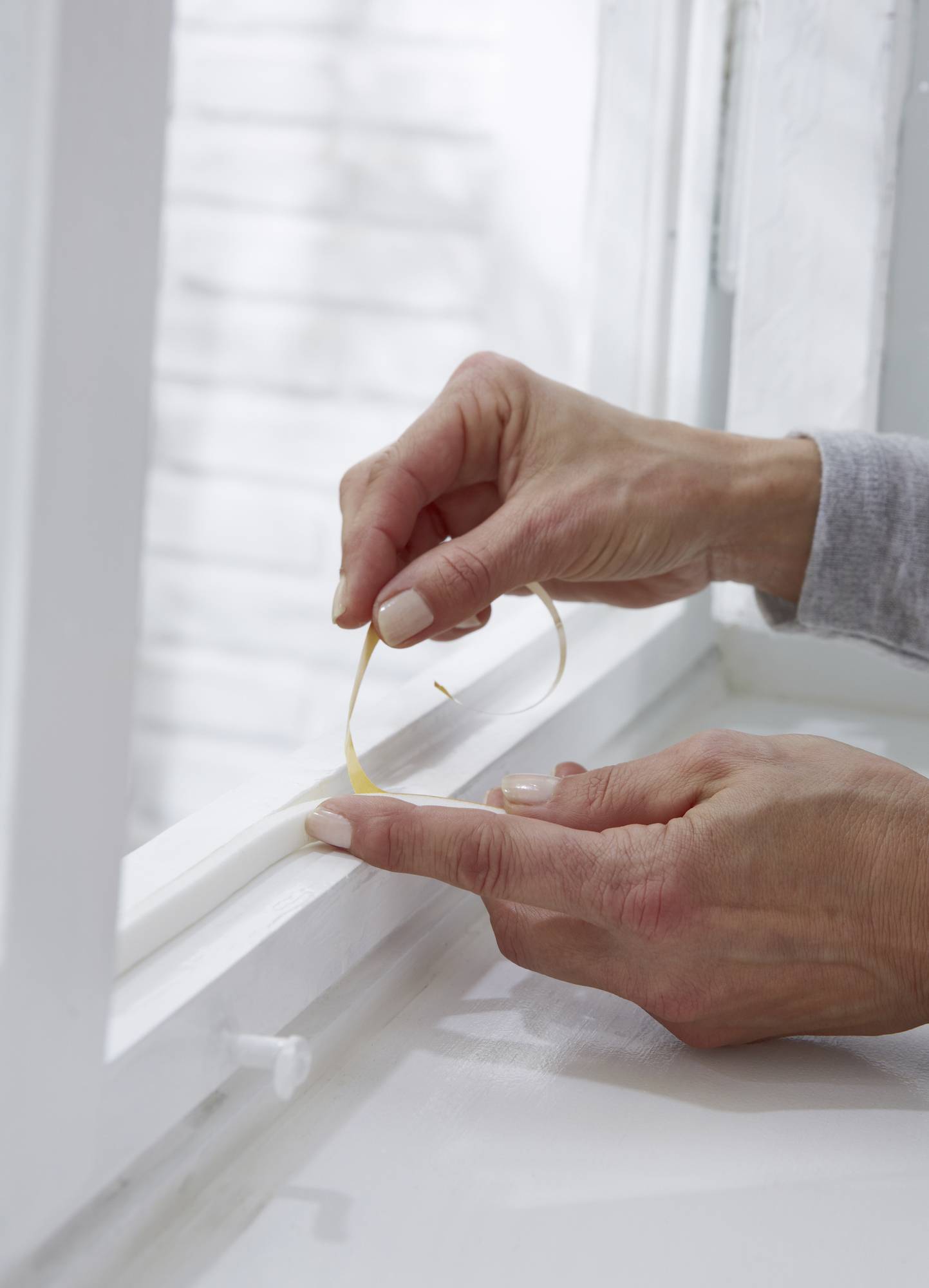 Eine Person bringt Dichtungsband an einem Fensterrahmen an, um Zugluft zu verhindern.