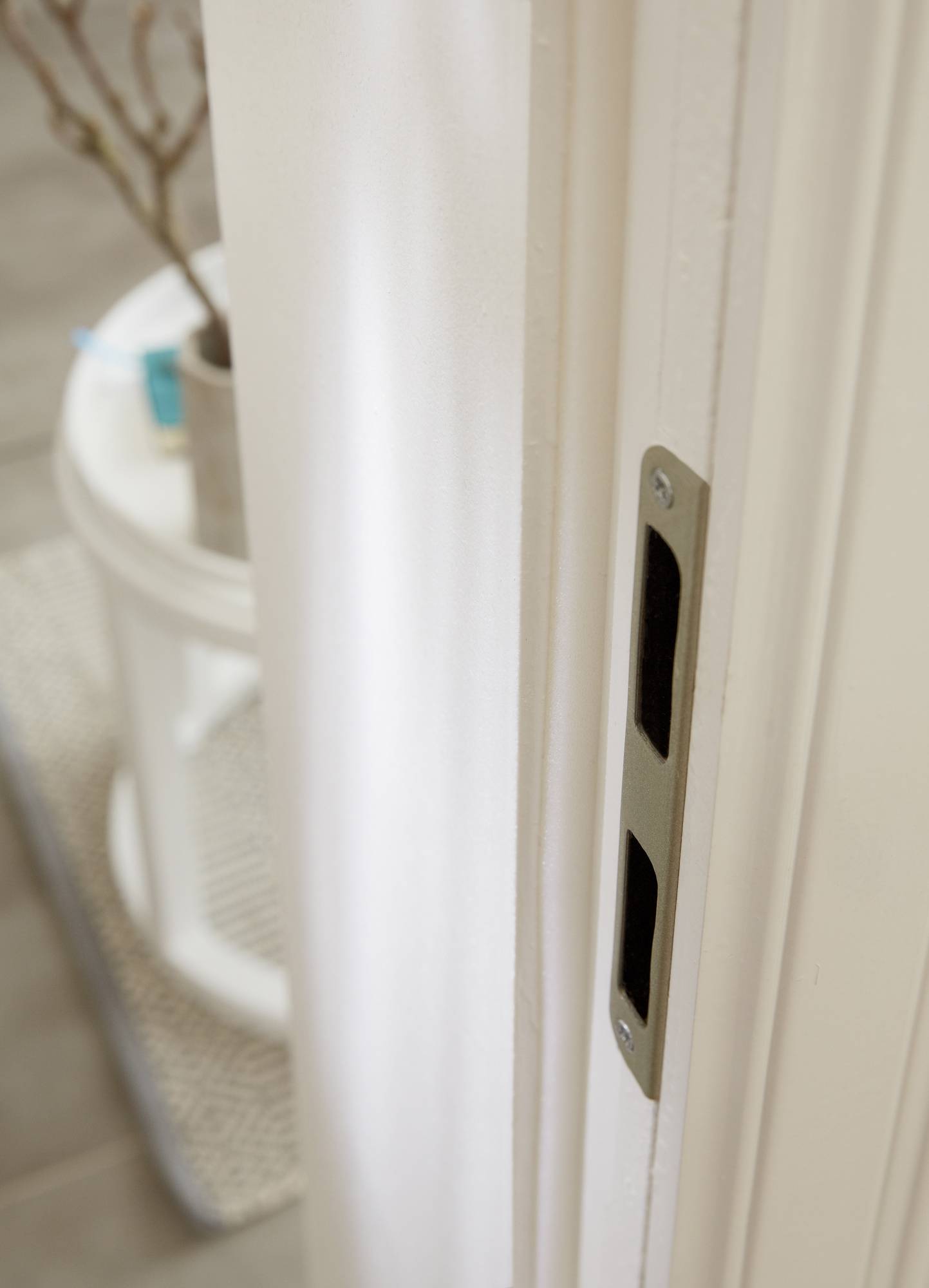 Türrahmen mit Aussparung für ein Türschloss, unscharfer Hintergrund mit Teil eines runden Tischs und dekorativem Zweig.