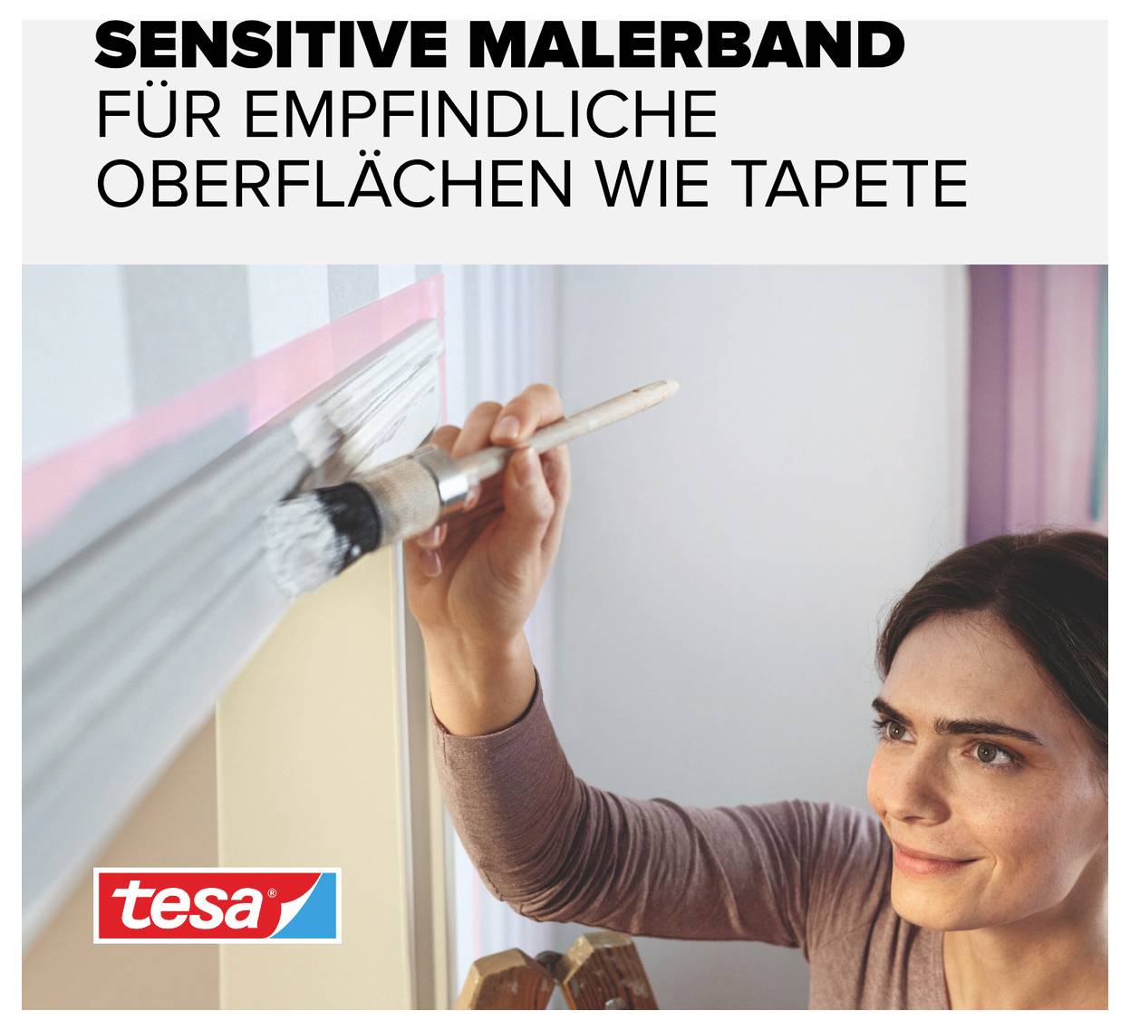 Eine Frau streicht mit einem Pinsel eine Wand, die mit 'sensitive Malerband für empfindliche Oberflächen wie Tapete' abgeklebt ist.