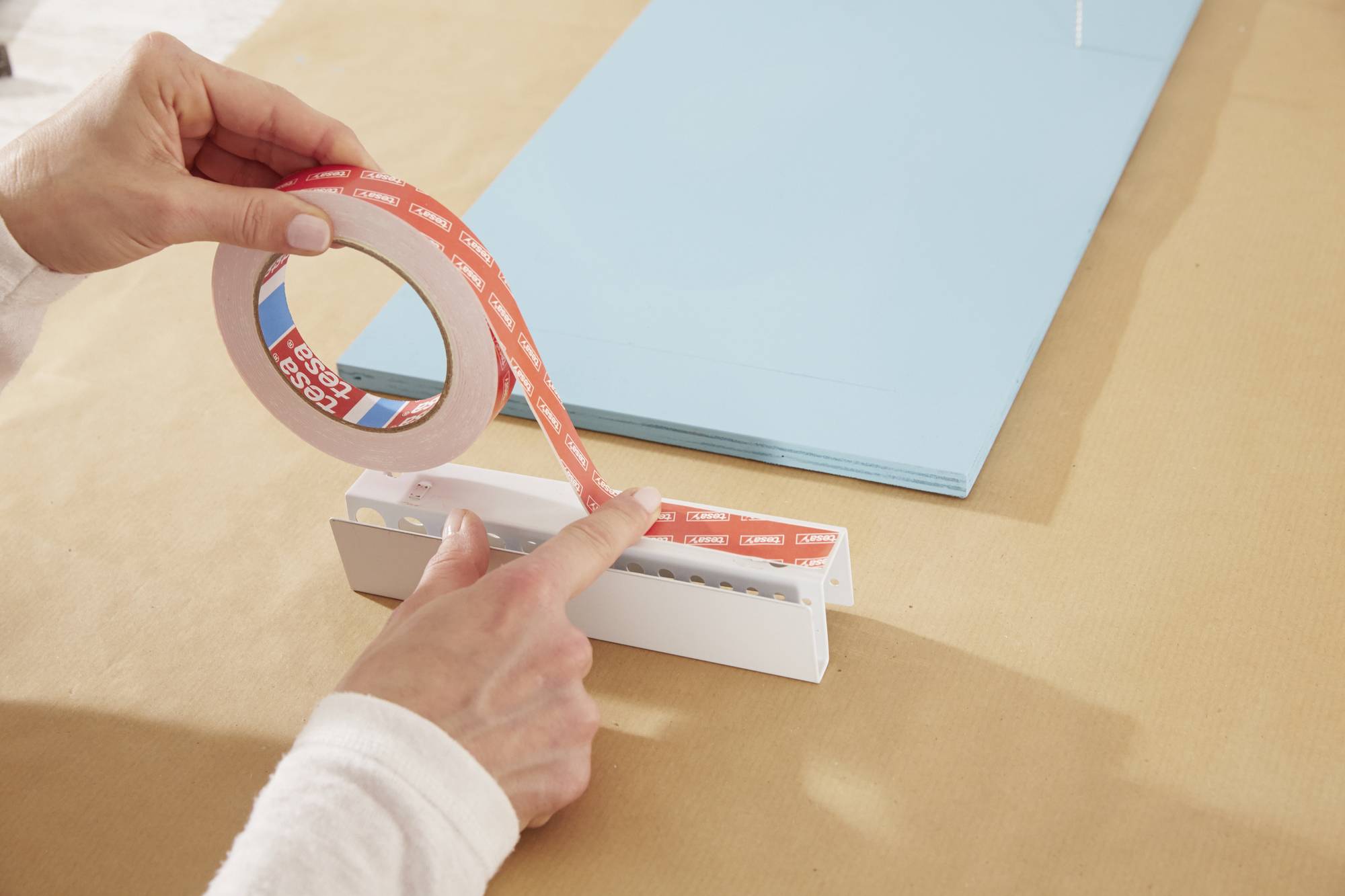 Eine Person befestigt ein doppelseitiges Klebeband auf einem Papierhalter, während blaues Papier daneben liegt.