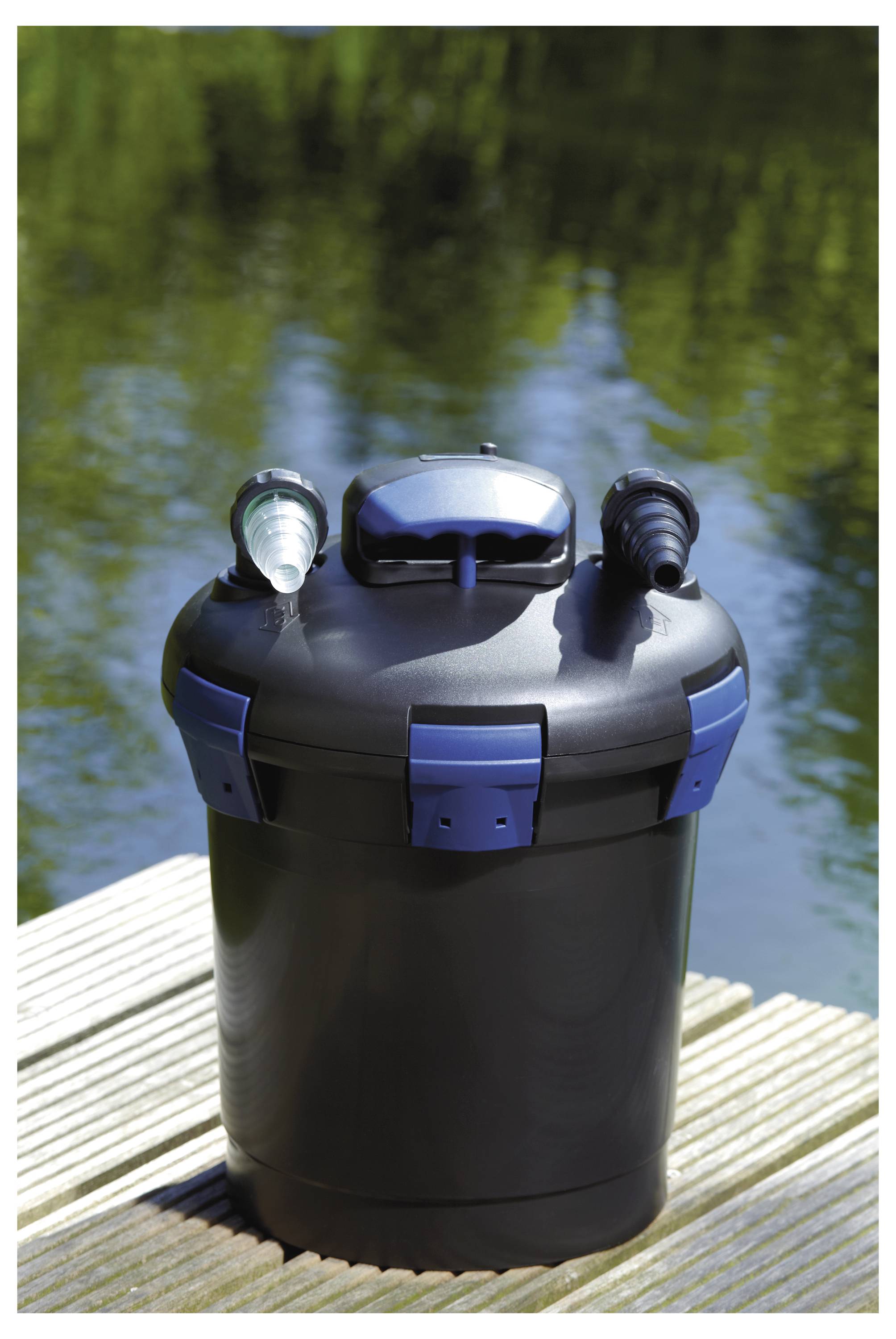 Ein schwarzer und blauer zylindrischer Wasserfilter mit zwei Anschlüssen auf einer Holzplattform in der Nähe eines Teichs.
