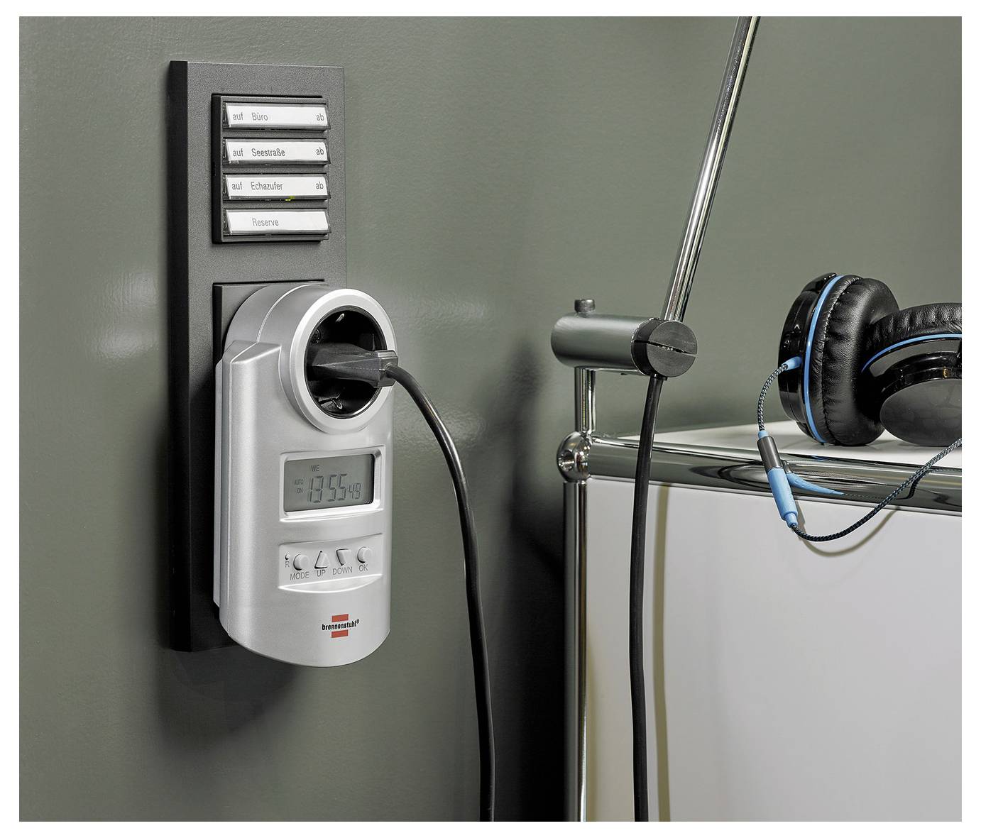 Kopfhörer, die neben einer an der Wand montierten Steckdosenleiste mit Zeitschaltuhr hängen, mit eingestecktem Stecker und einem kleinen digitalen Display.