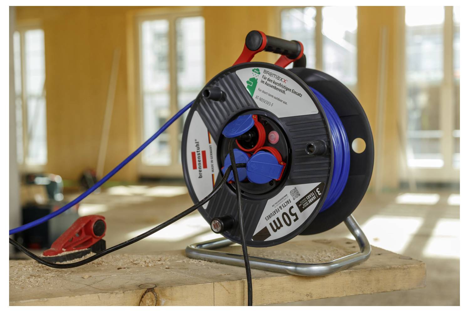 Ein blaues Verlängerungskabel auf einer Spule liegt auf einer Holzoberfläche in einem sonnendurchfluteten Raum und deutet auf laufende Bau- oder Renovierungsarbeiten hin.