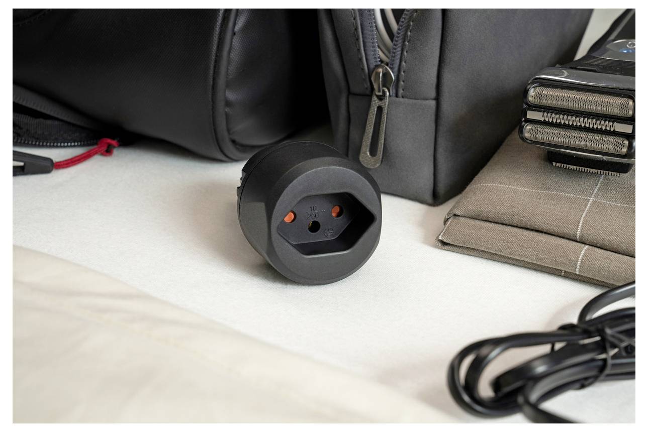 Nahaufnahme eines schwarzen universellen Stromadapters/Steckers mit Reisezubehör und aufgewickeltem Kabel auf einem Schreibtisch.