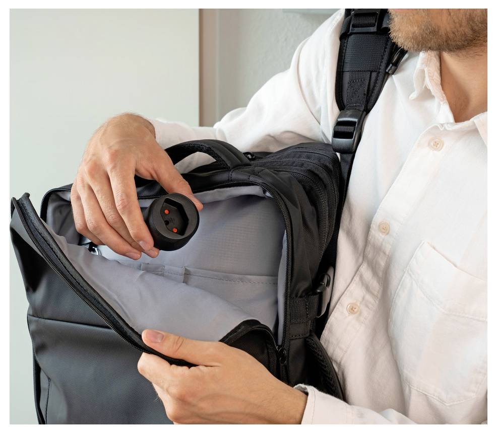 Mann hält einen schwarzen Rucksack offen und inspiziert ein verstecktes kreisförmiges Gerät im Inneren, was auf eine Kontrolle oder Sicherheitsüberprüfung hindeutet.