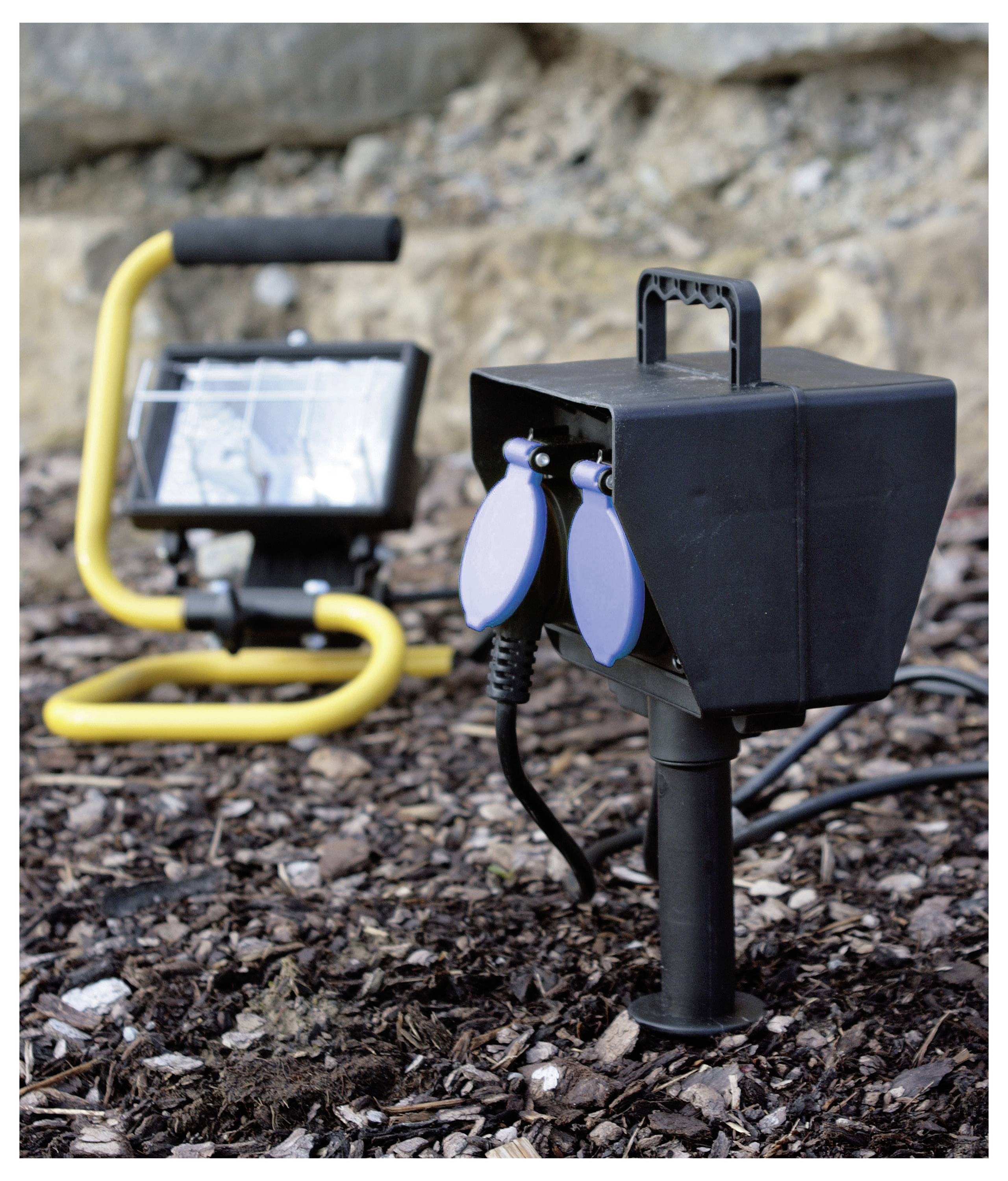 Eine solarbetriebene Außenstrahler mit einer schwarzen und blauen Steckdose ist in einer Gartenumgebung in den Boden gerammt.