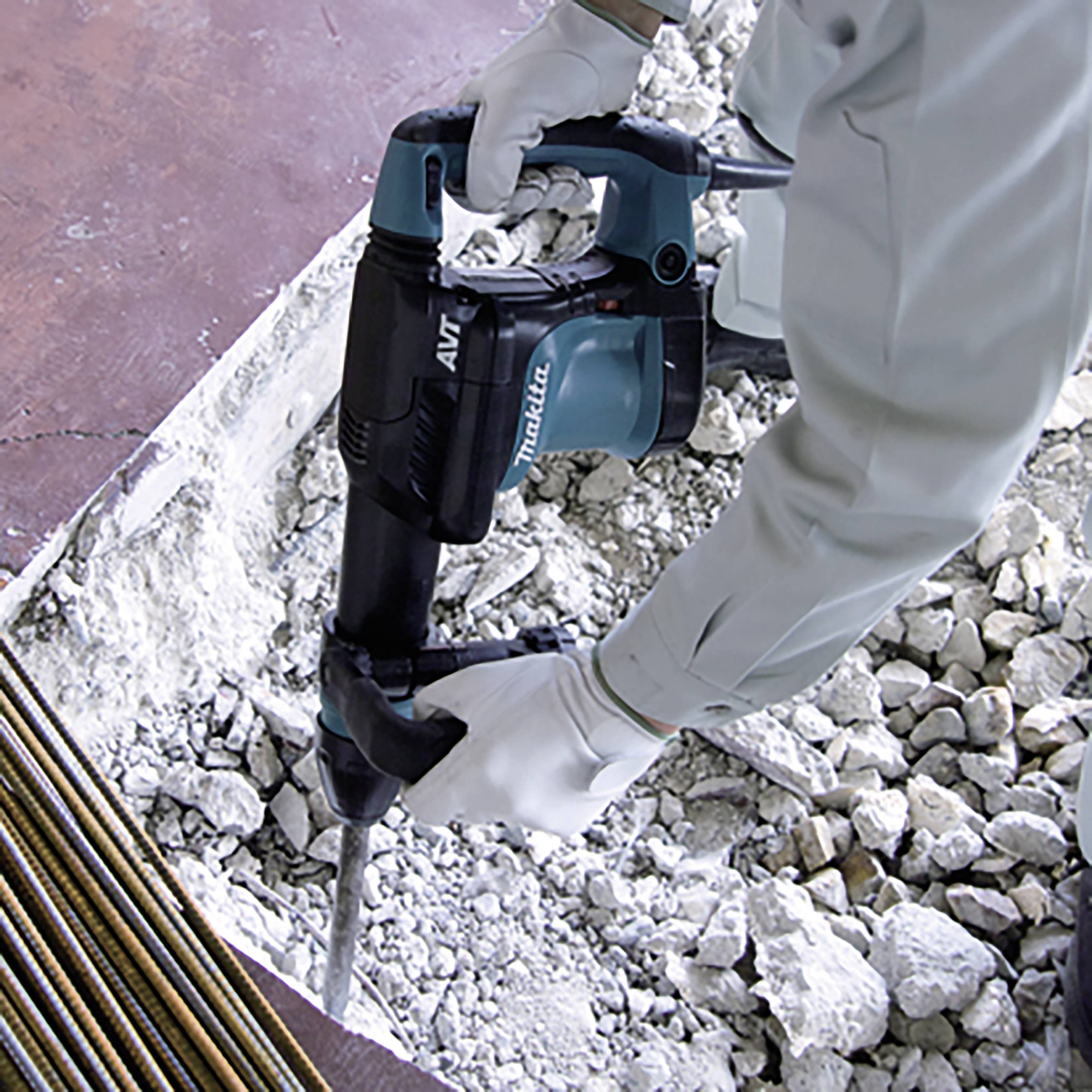 Eine Person in Schutzkleidung benutzt einen Bohrhammer, um Beton zu zerkleinern. Die Umgebung zeigt Schutthaufen und Metallstangen.