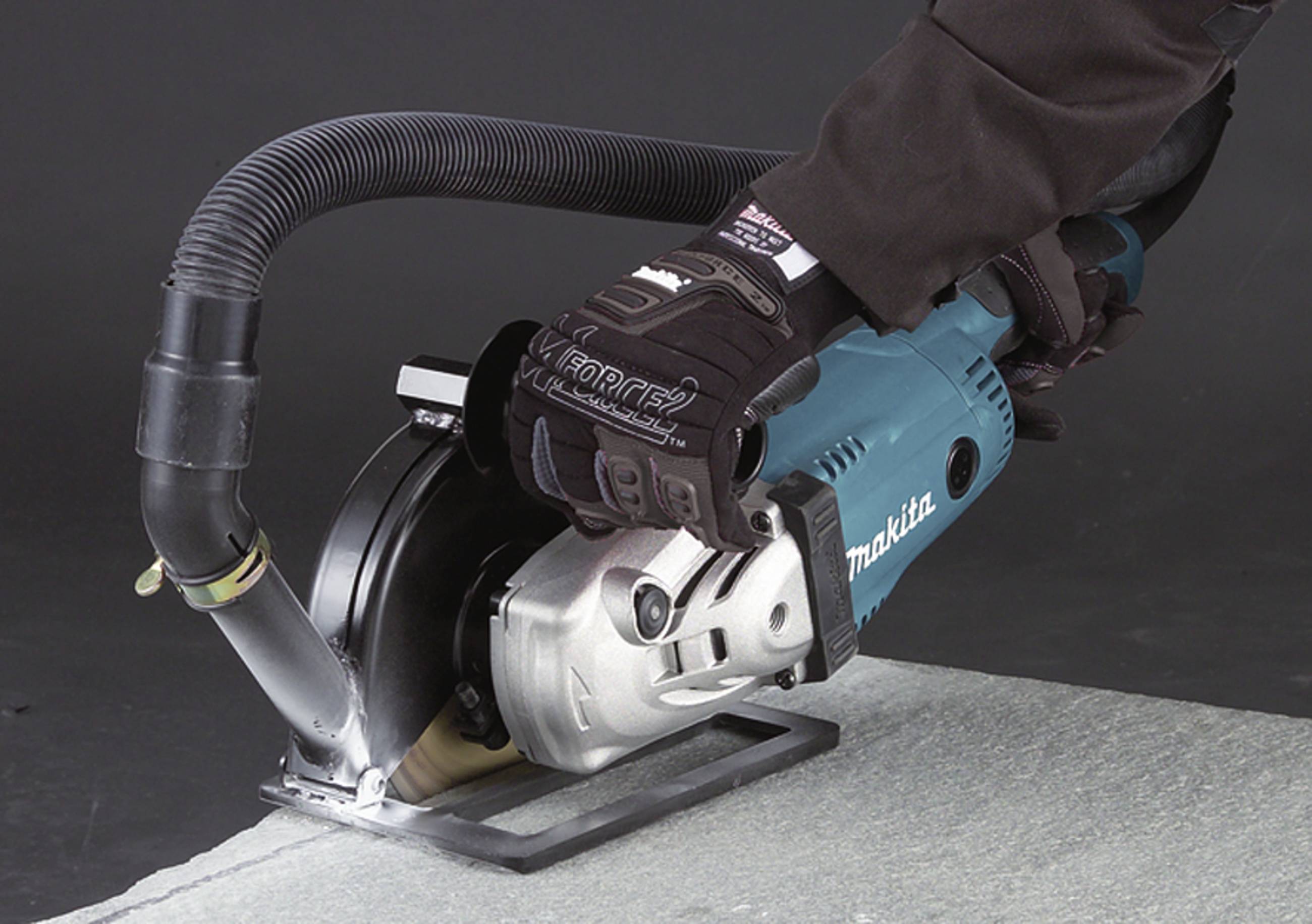 Eine Person schneidet mit einer blauen Elektrosäge ein graues Material. Die Säge hat eine Staubabsaugung. Handschuhe schützen die Hände.