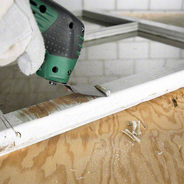 Eine Hand mit Handschuhen benutzt einen Akku-Schwingschleifer, um die Kanten eines Holzrahmens zu glätten. Im Hintergrund sind Kacheln zu sehen.