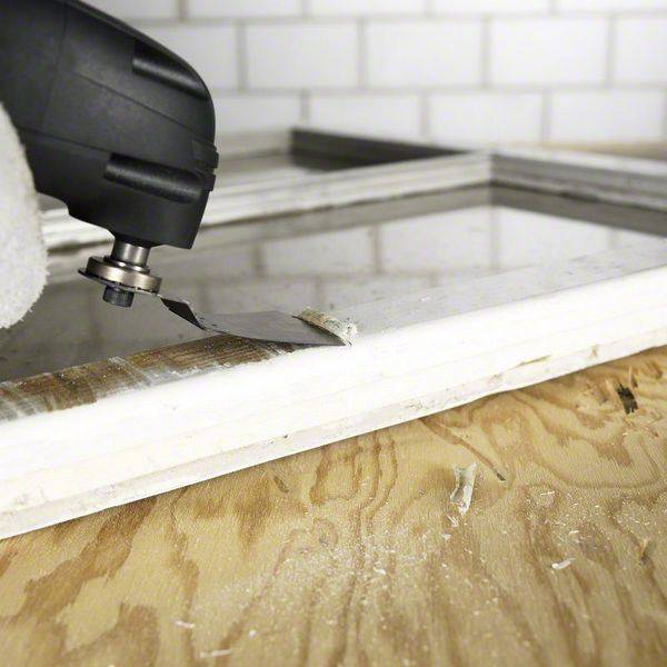 Ein Dremel-Multitool schneidet präzise durch Metall auf einem Holztisch in einer Werkstattumgebung.