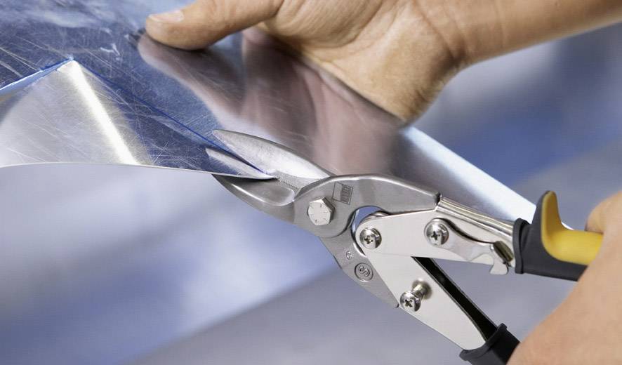 Eine Person schneidet mit einer Blechschere ein Stück Metall.
