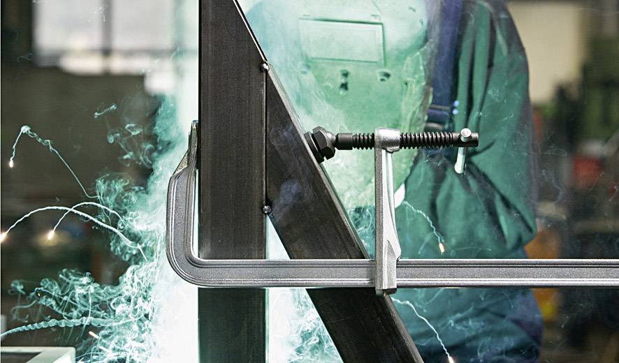 Eine Person schweißt ein Metallteil in einer Werkstatt. Funken fliegen und die Person trägt einen Schweißhelm zum Schutz.