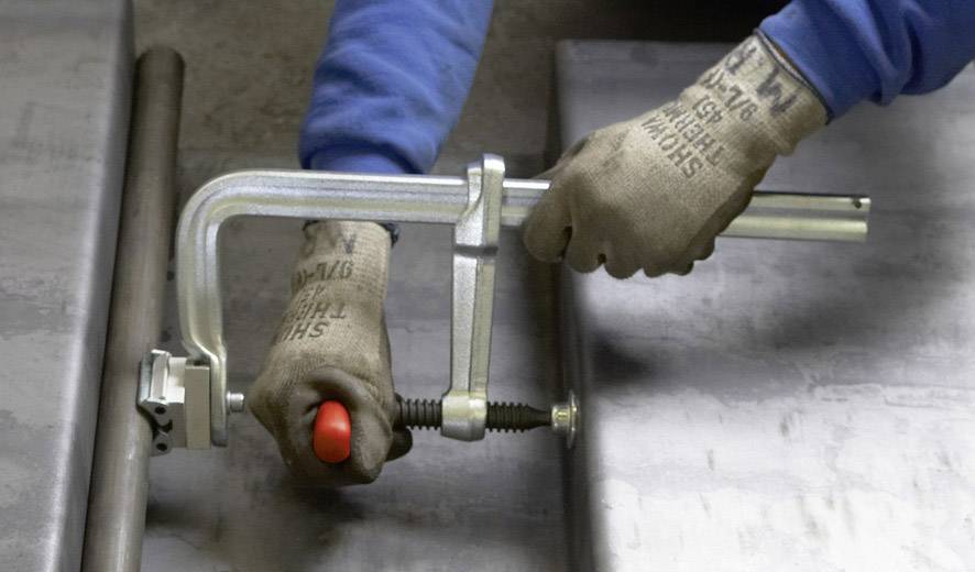 Arbeiter in blauen Ärmel und Handschuhen verwendet eine Klemme, um zwei Metallplatten zusammenzudrücken. Konzentration auf Präzision.