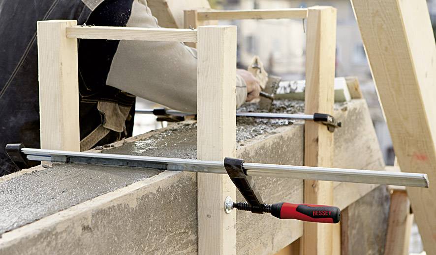 Eine Person glättet frisch gegossenen Beton in einer Holzschalung mit einem Werkzeug für eine ebene Oberfläche.