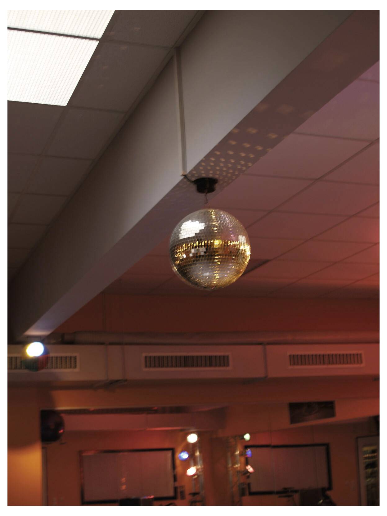 Disco ball hanging from a ceiling in a dimly lit room with warm red-orange lighting.