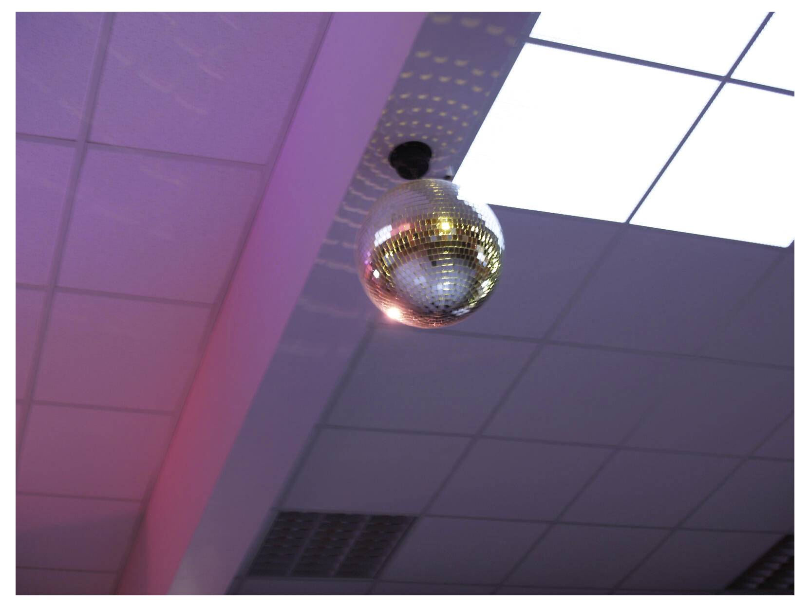 Ein verspiegelter Diskokugel hängt von der Decke unter lila und weißen Lichtern.