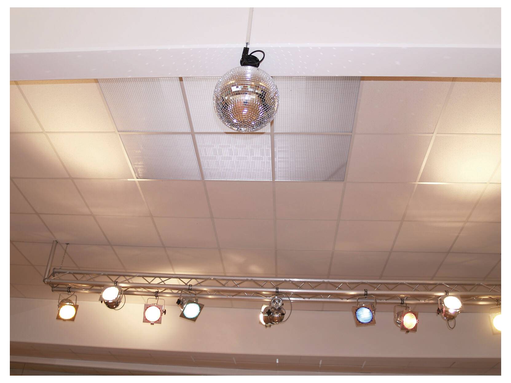 Decke mit einer kleinen Diskokugel und einer Reihe von Bühnenscheinwerfern auf einem Metallträger in einem Innenraum.