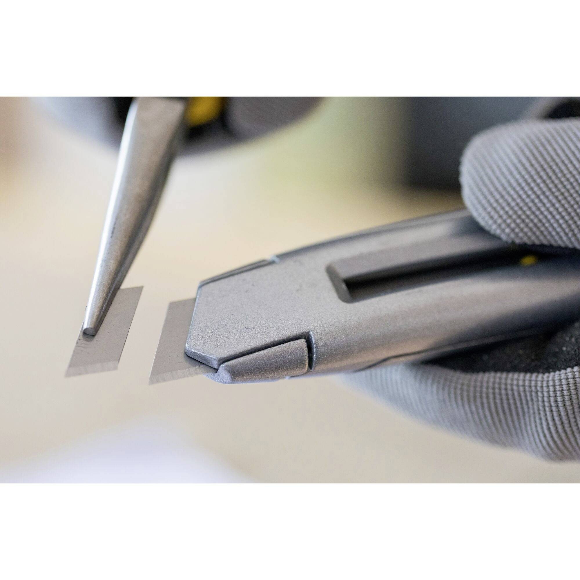 Eine Nahaufnahme von Händen in Handschuhen, die mit Werkzeugen arbeiten, zeigt präzises Schneiden eines kleinen rechteckigen Materials.
