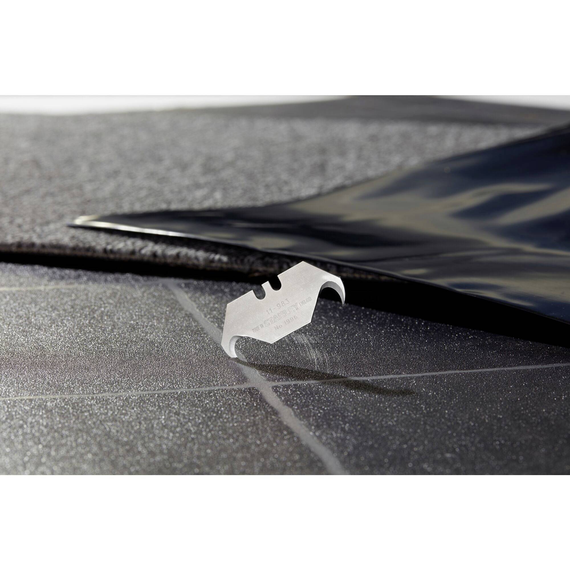 Ein Rasierklingenmesser liegt auf schwarzem, körnigem Material, das teilweise von einer glänzenden Folie bedeckt ist.