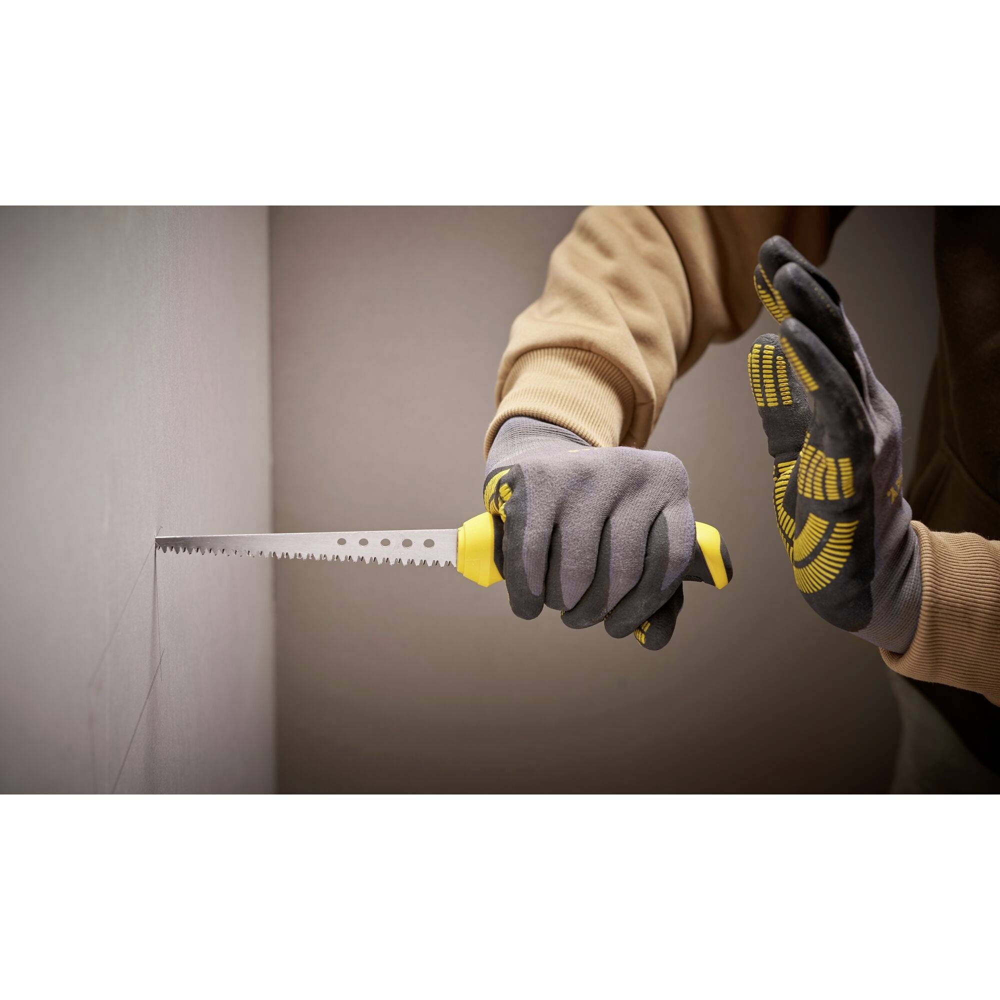 Eine Person schneidet mit einer Handsäge ein Loch in eine Wand. Sie trägt graue Handschuhe.