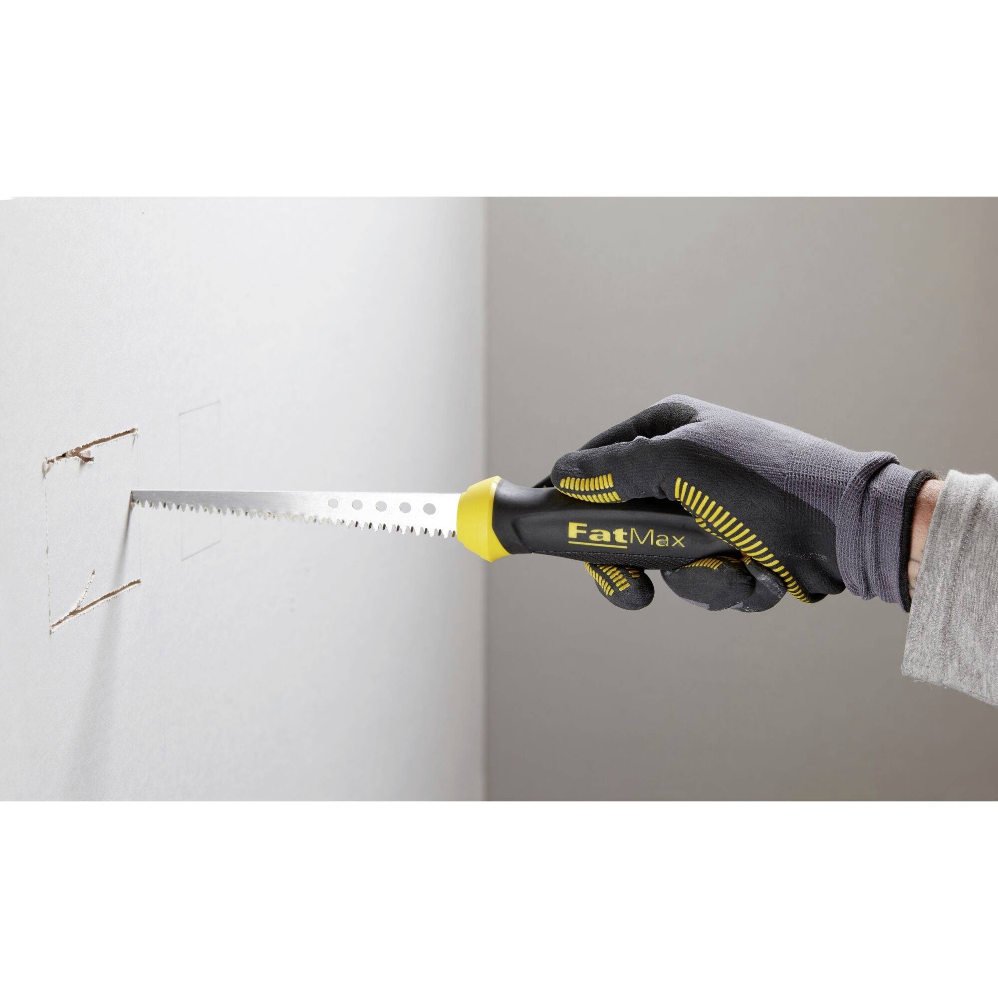 Eine Person schneidet mit einer Handsäge ein Rechteck in eine Gipskartonwand. Sie trägt einen Handschuh und hält das Werkzeug fest.