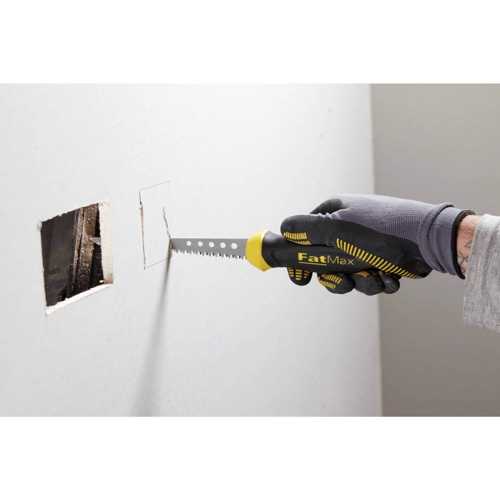 Eine Person schneidet mit einer Handsäge ein quadratisches Loch in eine Gipskartonwand.