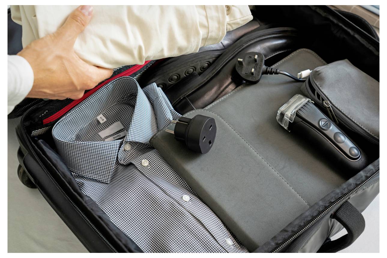 Offener Koffer mit einem Hemd, schwarzem Rucksack und elektronischen Geräten, was organisierte Geschäftsreisen andeutet.