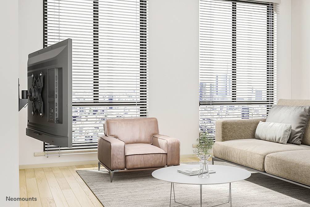 Ein Wohnzimmer mit einem beigefarbenen Sofa, einem rosafarbenen Sessel, einem runden Couchtisch und einem an der Wand montierten Flachbildfernseher.