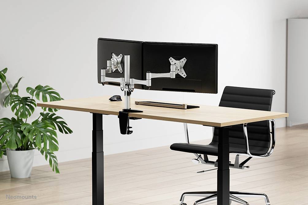 Moderner Schreibtisch mit zwei Monitoren, verstellbarer Halterung und ergonomischem Stuhl, auf einem hellen Holzboden. Pflanze im Hintergrund.