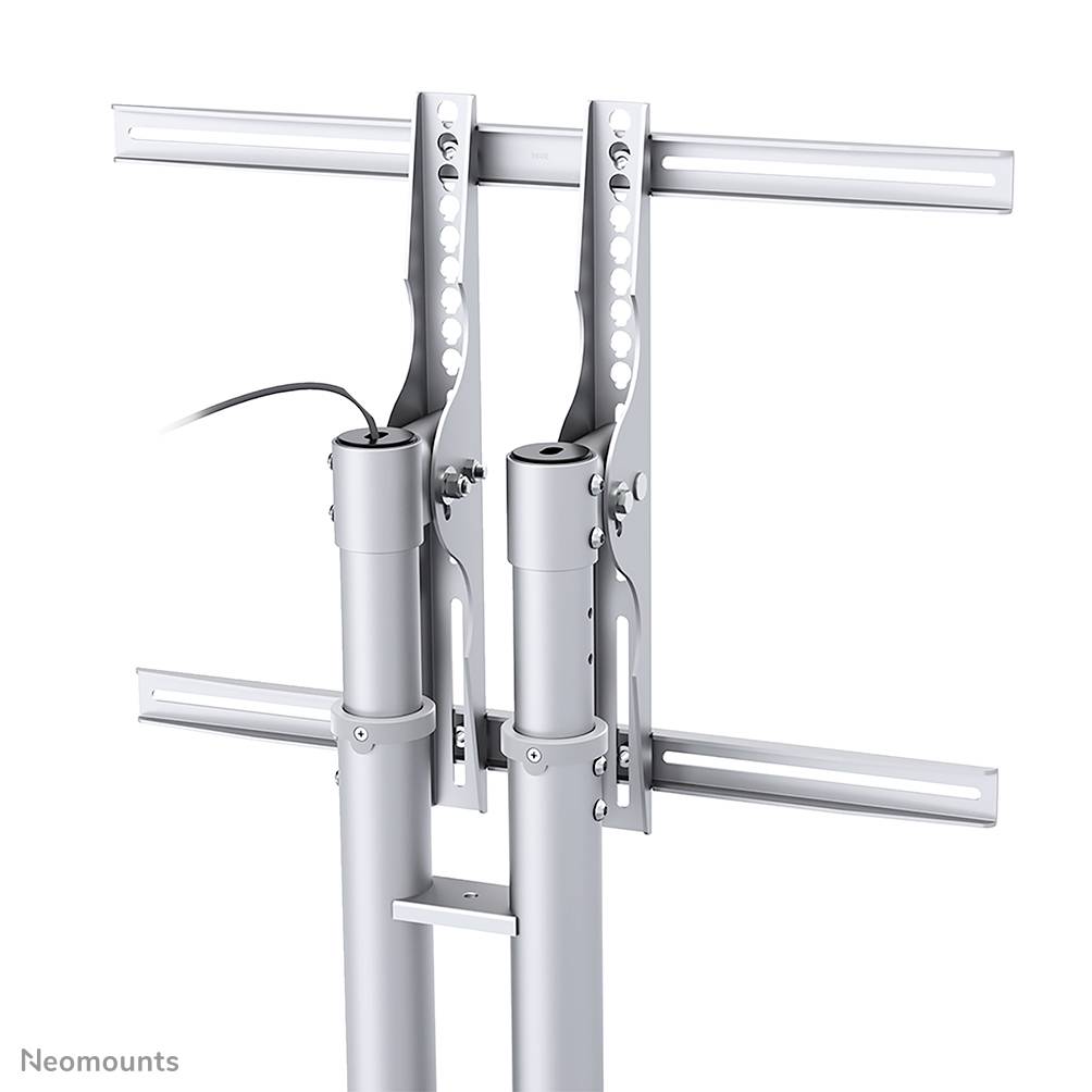 Zwei silberne Halterungen mit einstellbaren Armen für Monitore oder Bildschirme, montiert auf vertikalen Säulen. Kabel sichtbar.