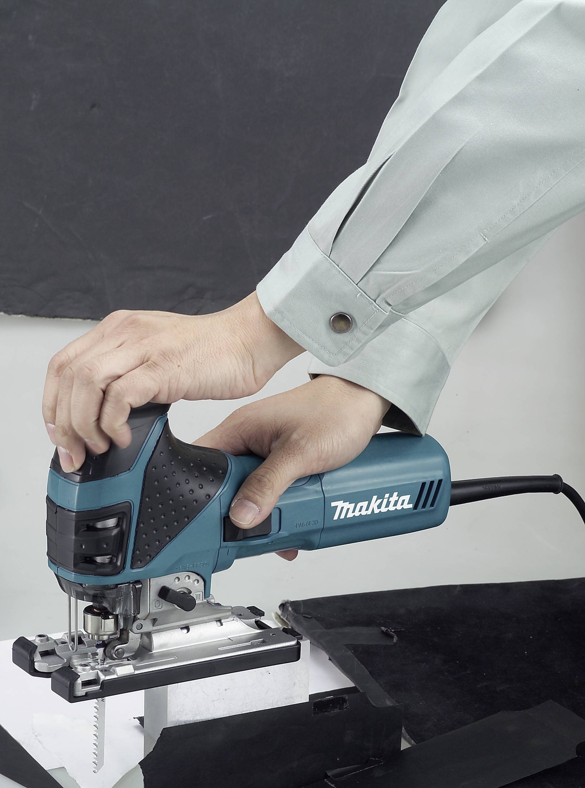 Eine Person hält eine elektrische Stichsäge der Marke Makita und schneidet damit durch ein Material auf einer Werkbank.