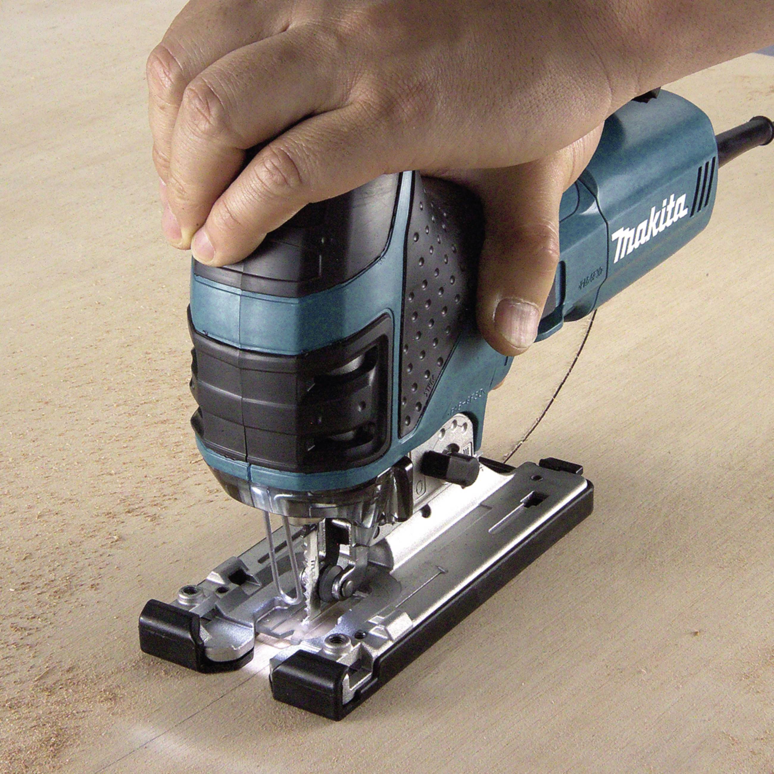 Eine Hand hält eine elektrische Stichsäge und schneidet präzise Holz. Staubpartikel sind sichtbar, während die Säge arbeitet.