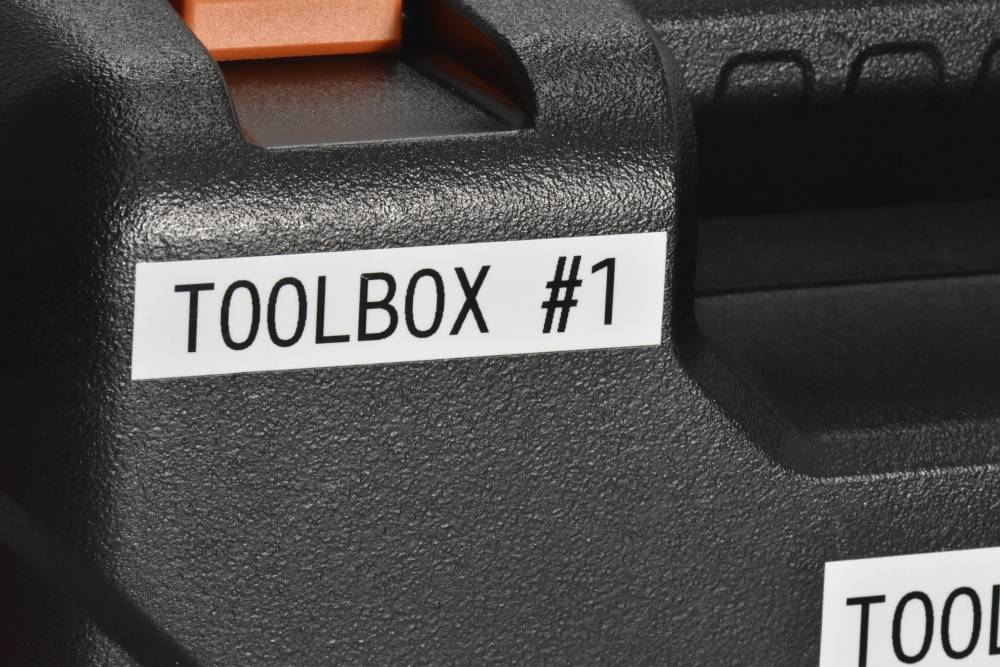 Schwarzer Werkzeugkasten mit einem Etikett, auf dem 'TOOLBOX #1' steht. Oben links ist ein orangefarbener Griff erkennbar.
