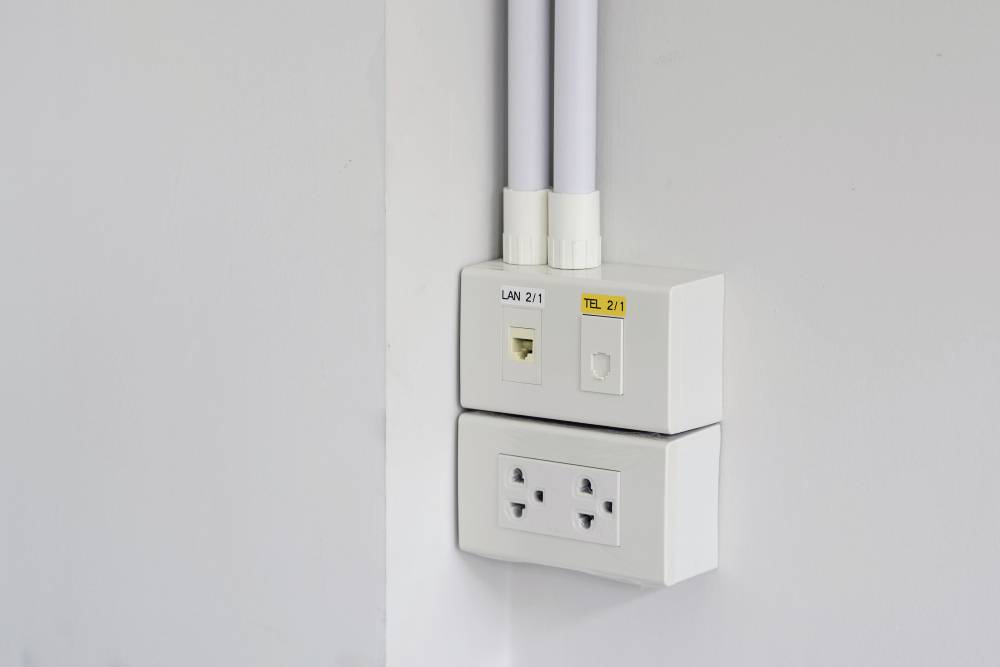 Eine Wandsteckdose mit zwei Steckplätzen und daneben Anschlüsse für LAN und Telefon, montiert an einer weißen Wand.